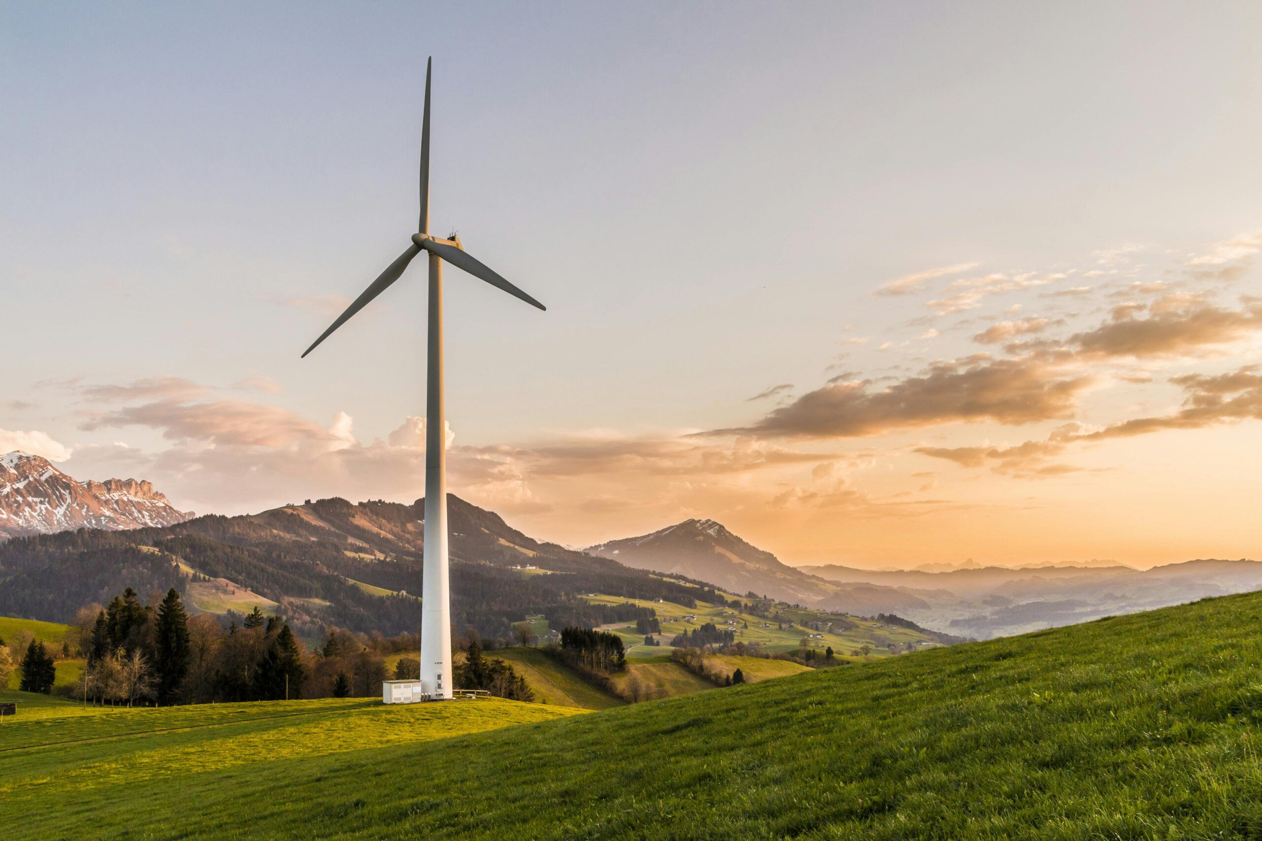 pexels-photo-414837-414837-1 Wind turbine amid rolling hills and mountains at sunset, symbolizing renewable energy and sustainability.